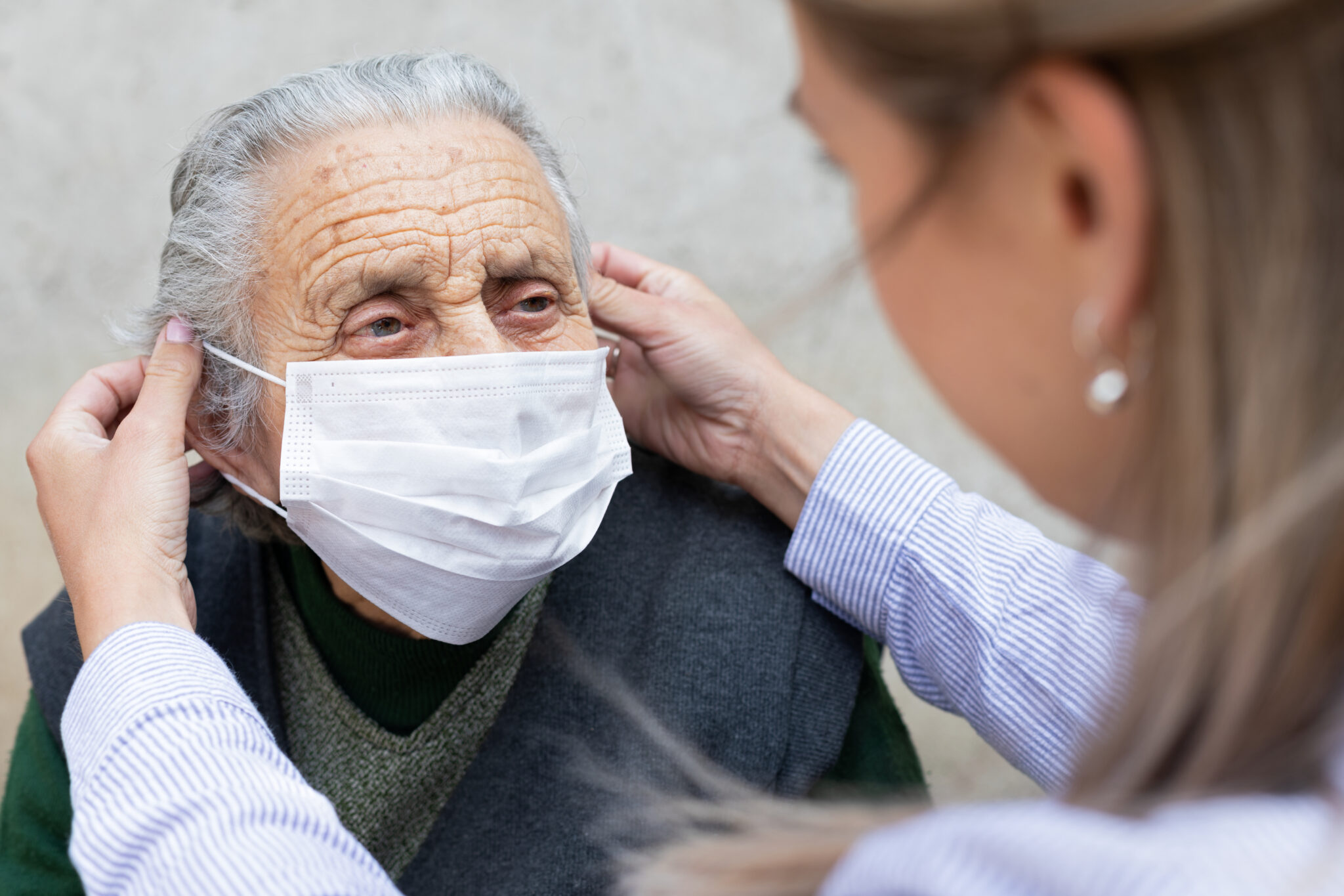 woman putting mask on old lady
